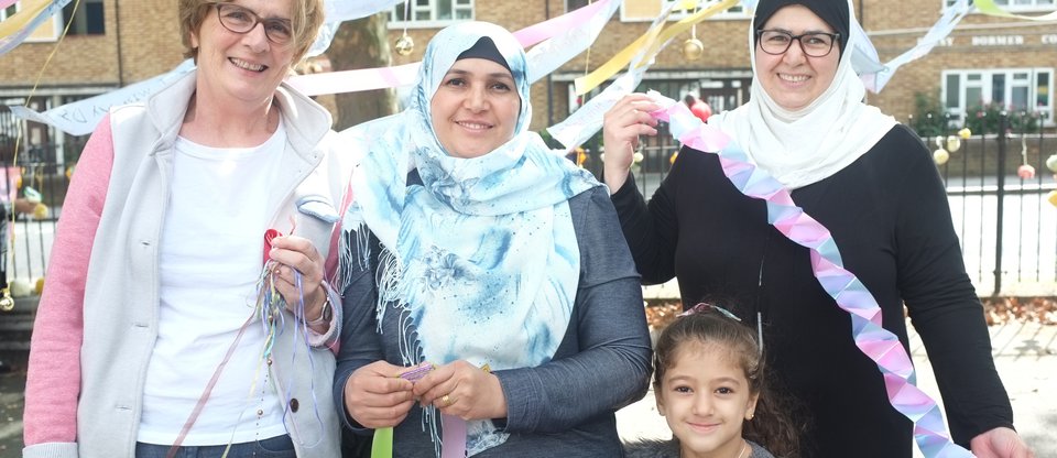Group photo of women and a young girl in a school playground holding banners and ribbons whilst smiling at refugee welcome event