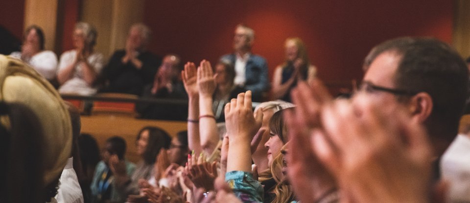 Lots of people in a room clapping with hands raised in the air