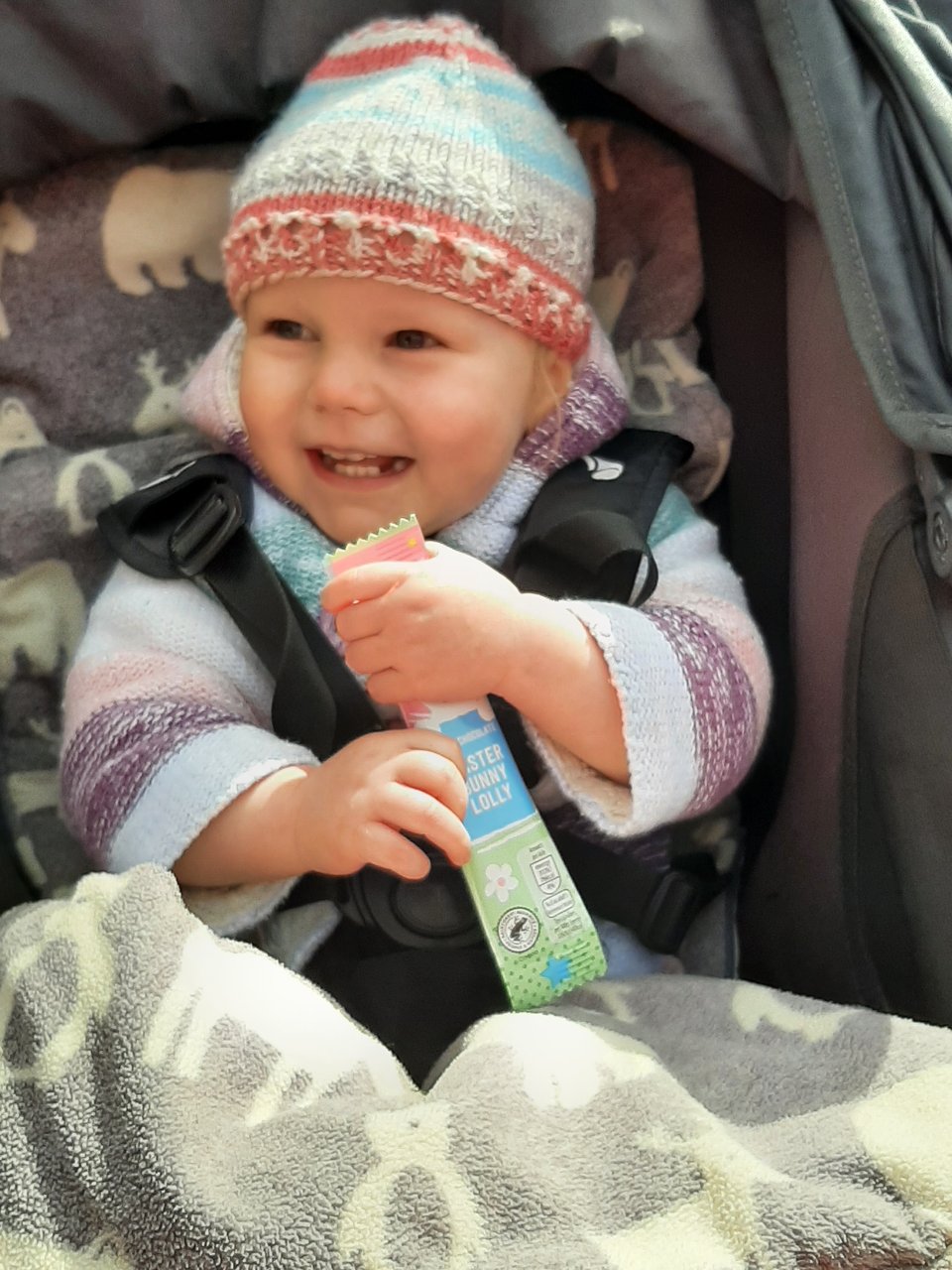 Baby smiling in its pram while holding a lolly.
