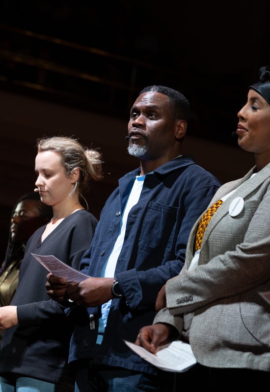 A Citizens UK leader on stage, sharing testimony amongst a group of people