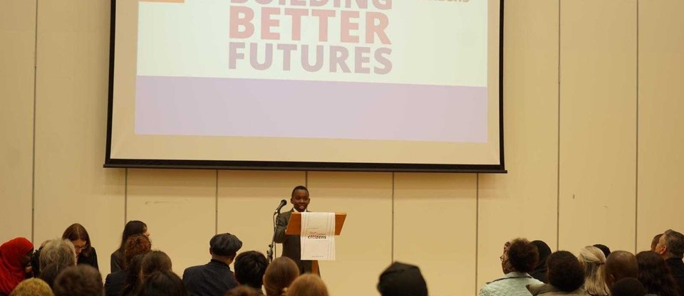 A pupil is speaking on stage in front of an audience and behind him is a screen with the Building Better Futures name.