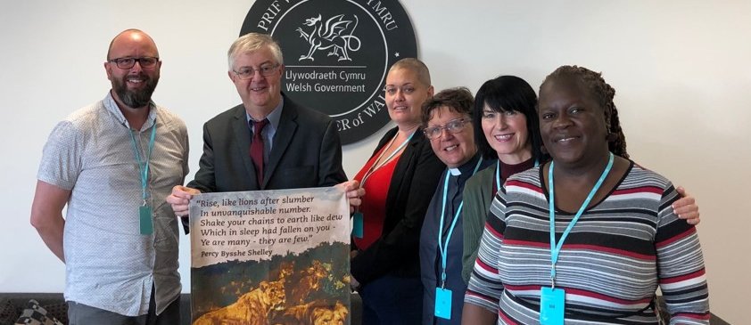 Five community leaders from Citizens Cymru Wales stand smiling with Mark Drakeford, First Minister of Wales.