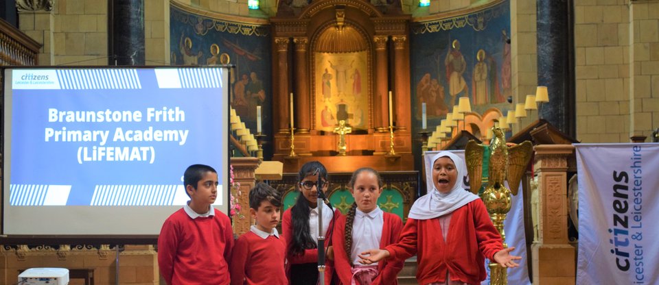 Five young students speak in church hall passionately about refugee welcome school accreditation