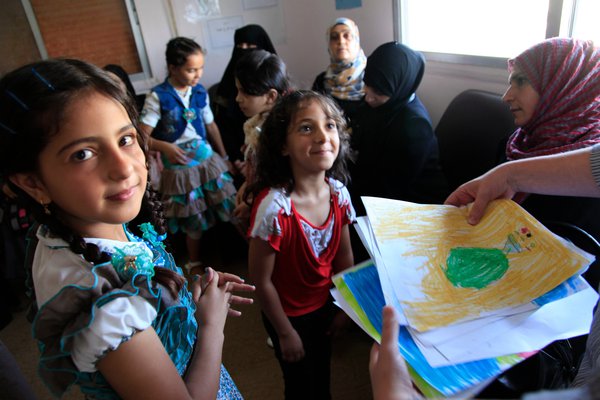 Young refugee children smiling and handing in drawings