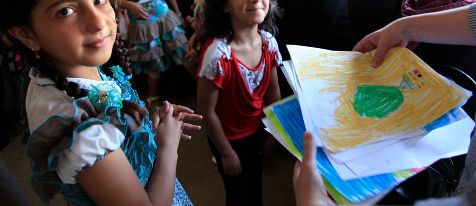 Young refugee children smiling and handing in drawings