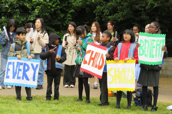 Children and community leaders from Citizens UK stand during a protest outside Parliament, holding colourful banners that say 'Every child should benefit'