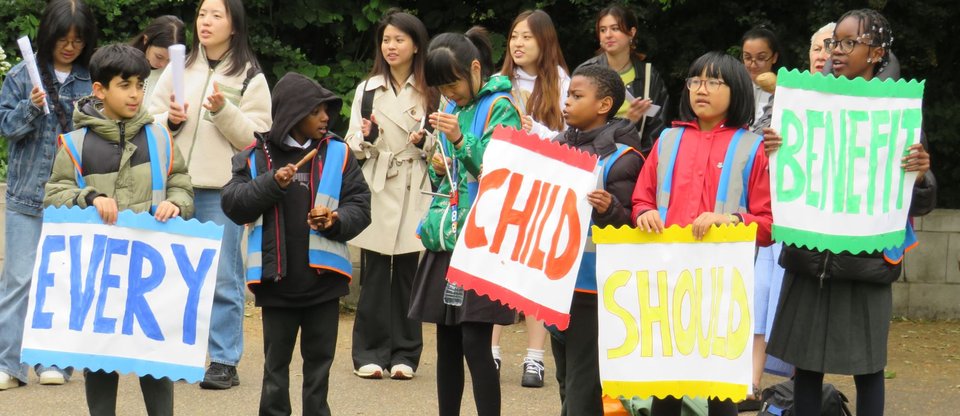 Children and community leaders from Citizens UK stand during a protest outside Parliament, holding colourful banners that say 'Every child should benefit'