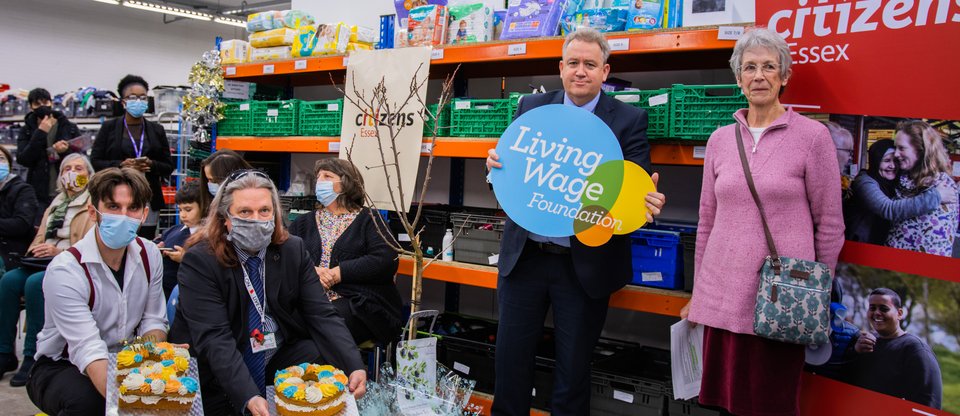 A group of people celebrating the Living Wage by holding up decorated cakes and logos for the Living Wage Foundation