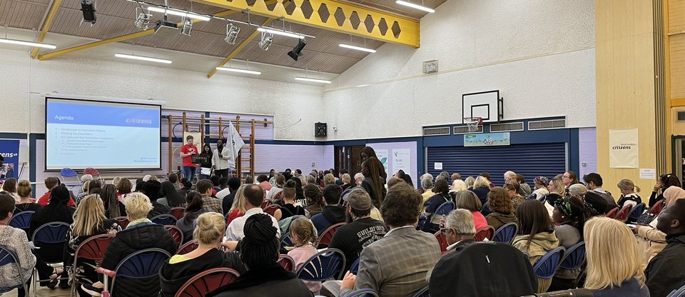 People sit in rows at an assembly in gym hall watching a presentation