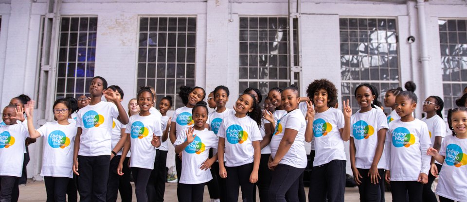 Newham Citizens student members, St Antony's choir, smiling and waving in Living Wage Foundation shirts, performing at Living Wage Week 2021