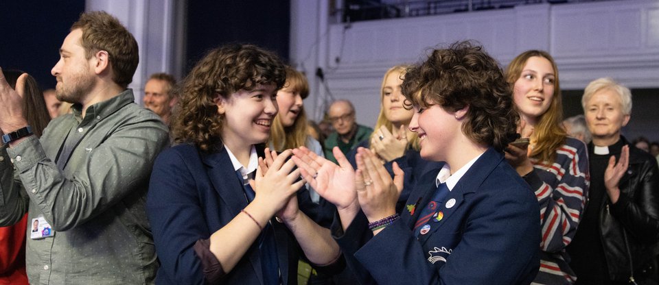 Two school children clapping and smiling at a Citizens UK assembly