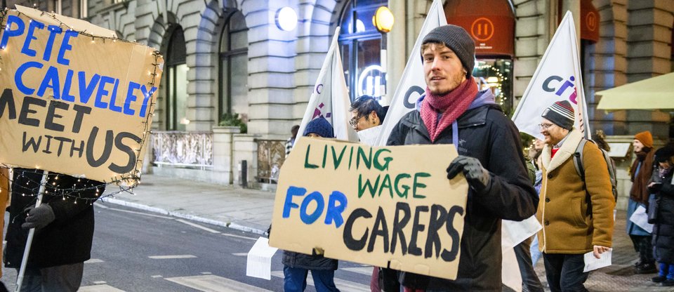 Leaders crossing the road with a Living Wage for Carers sign