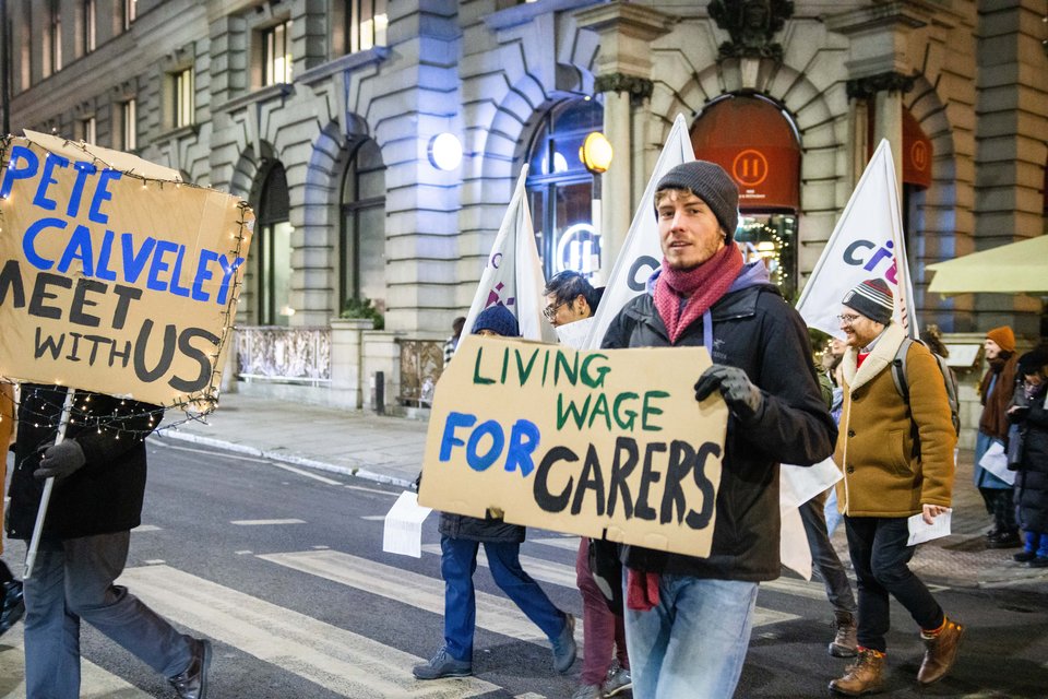 Leaders crossing the road with a Living Wage for Carers sign