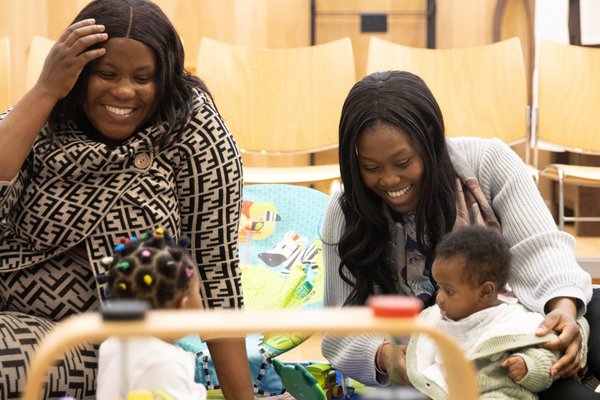 Two mums are smiling and playing with their toddlers.