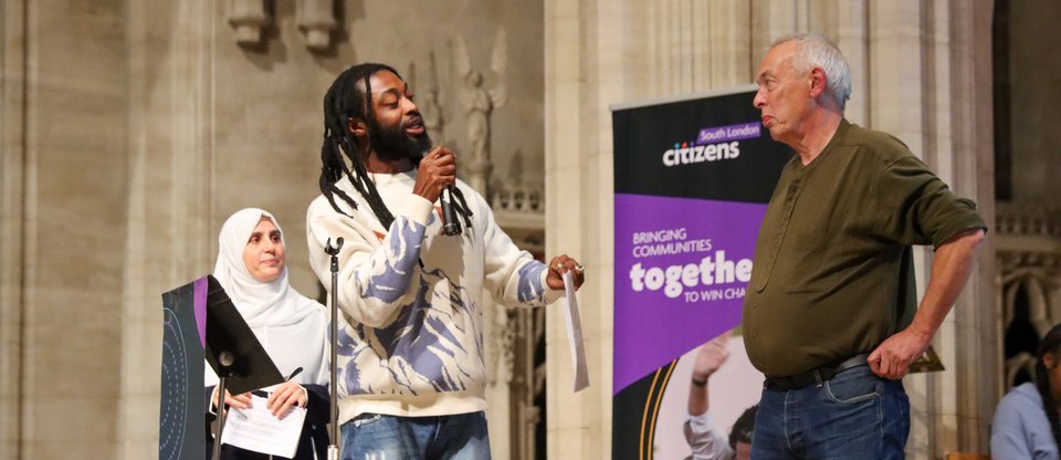 Two community leaders are on stage, one is speaking with a mic in his hand