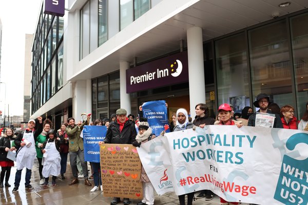 Campaigners stand outside Premier Inn with a large banner saying 'Hospitality workers for the real Living Wage' and 'Why not us'?
