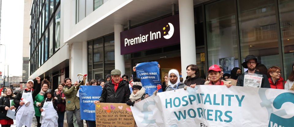 Campaigners stand outside Premier Inn with a large banner saying 'Hospitality workers for the real Living Wage' and 'Why not us'?