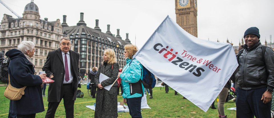 A group of Tyne and Wear community leaders are talking to an MP and holding a Tyne & Wear Citizens banner during a protest for the Living Wage Parliament Square.