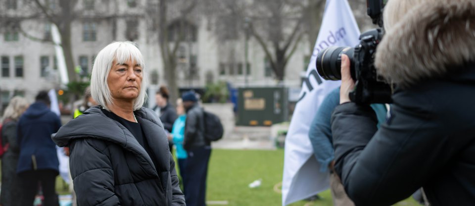 A care worker stands proudly in Parliament Square whilst a TV camera from the news films her interview.