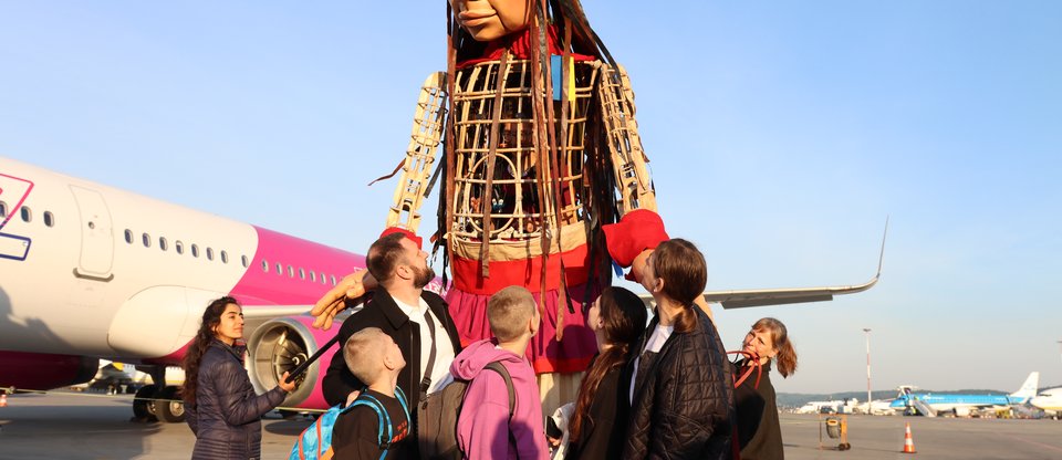 Ukrainian family of five look up at Little Amal, the giant Syrian refugee puppet, on airplane runway