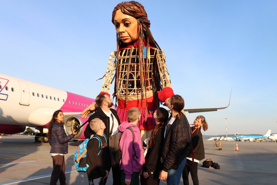 Ukrainian family of five look up at Little Amal, the giant Syrian refugee puppet, on airplane runway