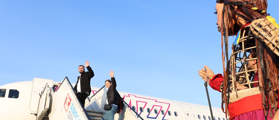 Man and woman wave at Little Amal, the Syrian refugee puppet, while boarding Whizz air flight