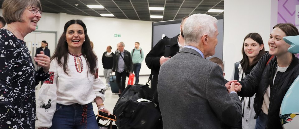 Man shakes hand of Ukrainian refugee at airport surrounded by host family and refugee family