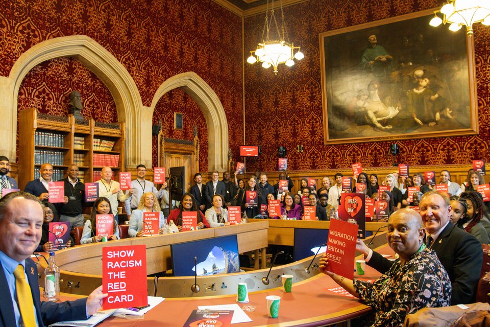 a group shot of people in a parliament room holding up red signs that say 'show racism the red card'