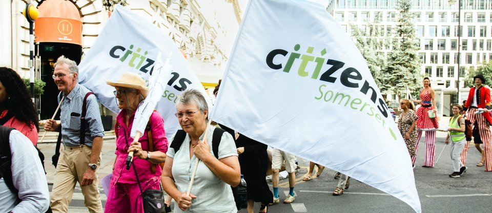Leaders holding Somerset Citizens flags crossing the road at an action targeting healthcare provider headquarters in London