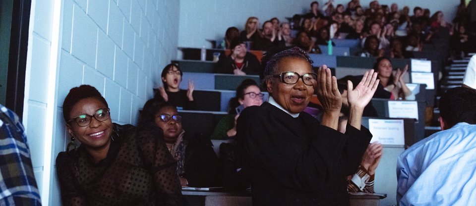 Community leader clapping and smiling at a South London Listens assembly