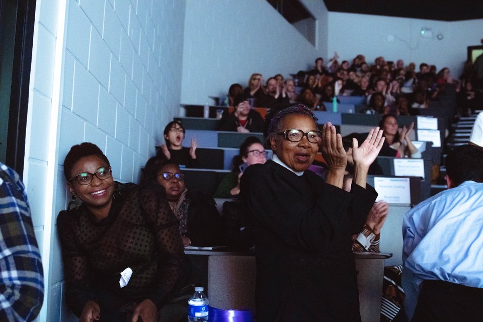 Community leader clapping and smiling at a South London Listens assembly