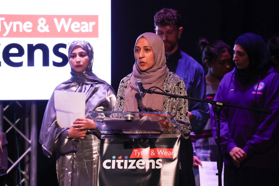 A woman is speaking at an assembly with Tyne & Wear Citizens logo