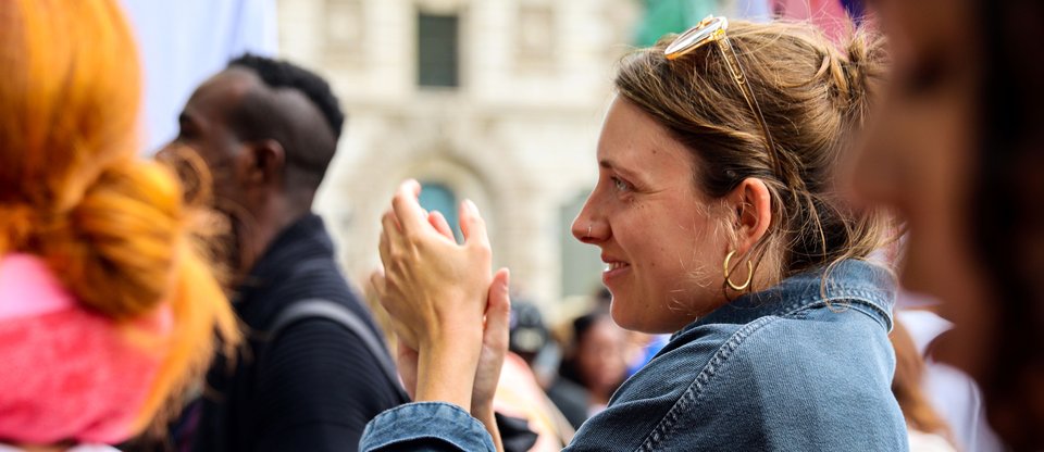 Close up shot of a person smiling and clapping in the middle of a crowd.
