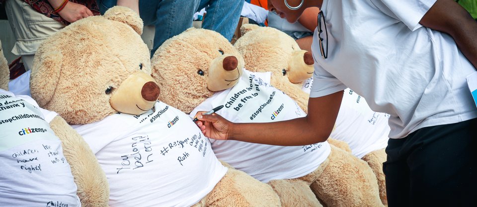 Person writing messages of hope on a giant teddy bear t-shirt, during an action in Parliament Square against the detention of refugee children.