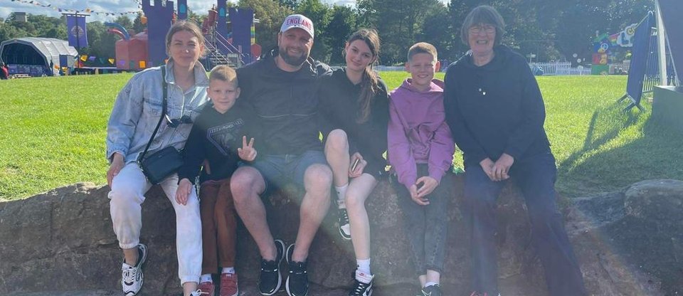 Family of five sit on a wall outdoors in front of a green space next to their host, Cora