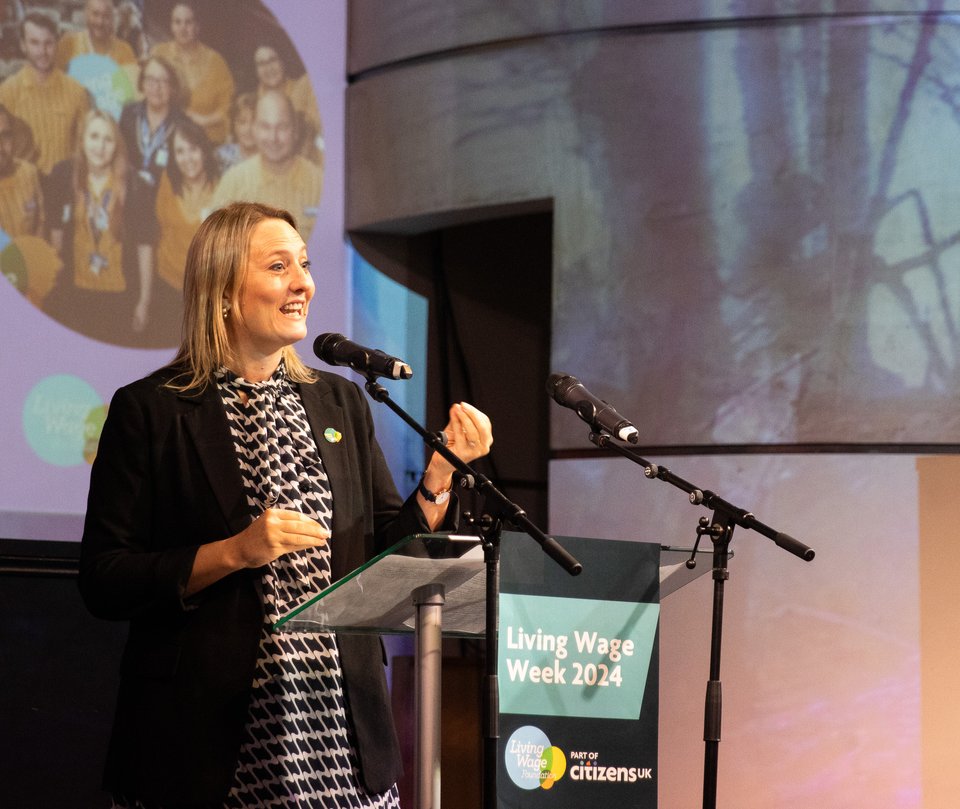 Katherine Chapman, Director of The Living Wage Foundation, is standing on stage giving a speech at a podium