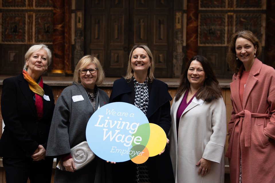 Katherine Chapman, Director of the Living Wage Foundation, stands holding up a sign which reads 'we are a Living Wage employer', alongside representatives for key accredited Living Wage businesses