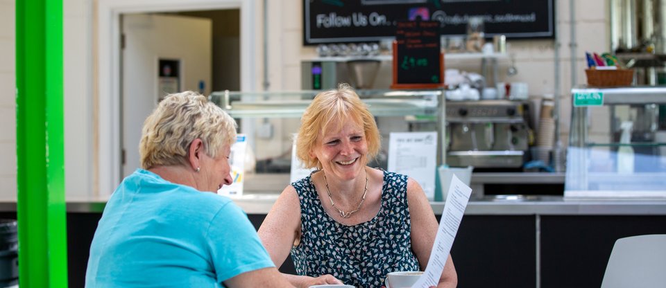 Two women sit around a table chatting and smiling over a cup of coffee.