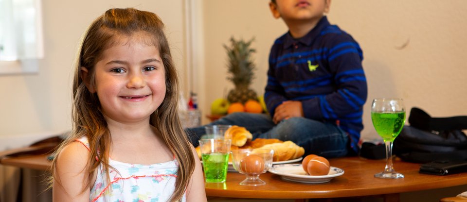 Two children smiling in their home with food and drinks on the table.