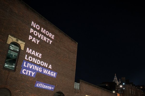 "No more poverty pay, making London a Living Wage city" is projected onto a wall with St Pauls in the background and people walking past