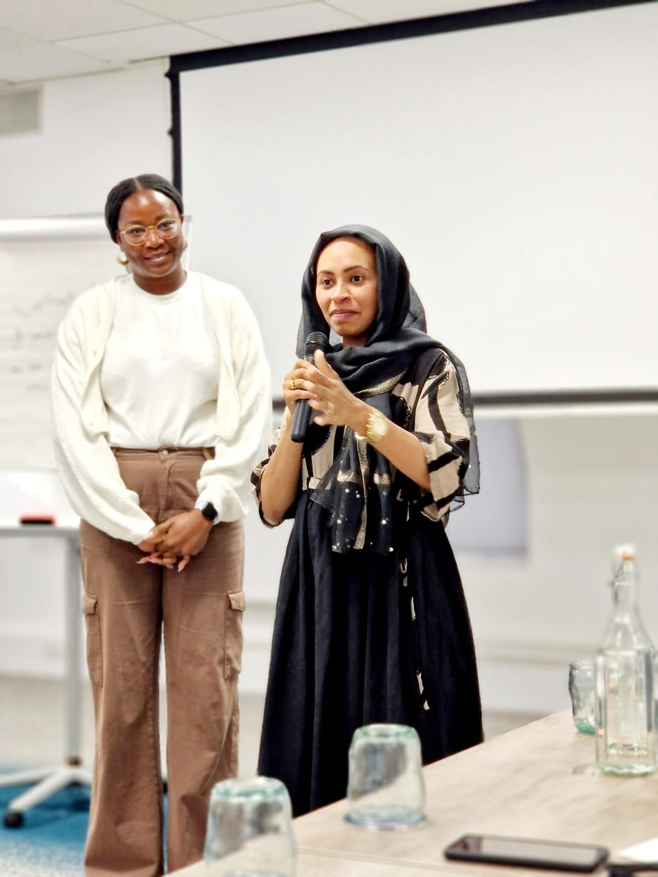 Mary Senjobi, Community Organiser for Redbridge Citizens, stands beside a leader sharing testimony at an action