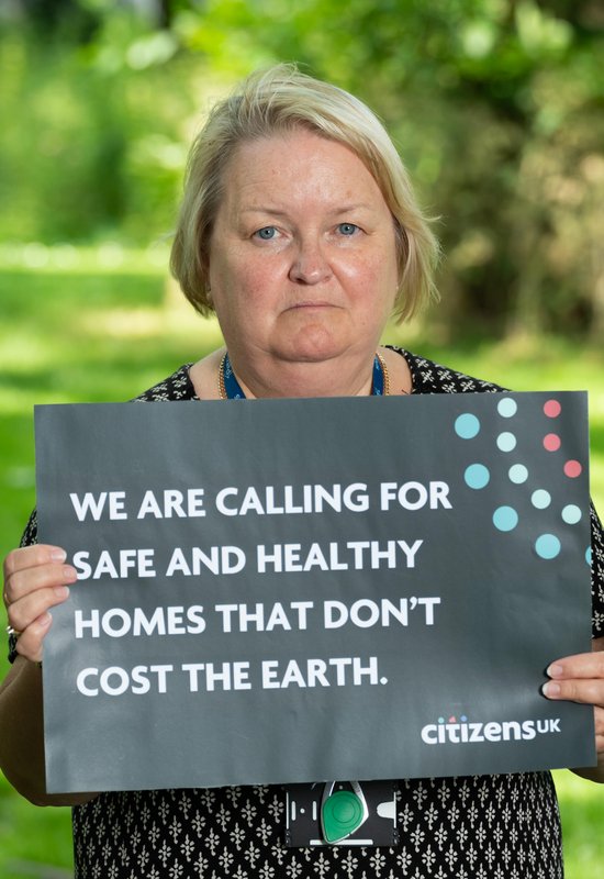 A community leader is holding a sign that reads 'We are calling for safe and healthy homes that don't cost the earth.'