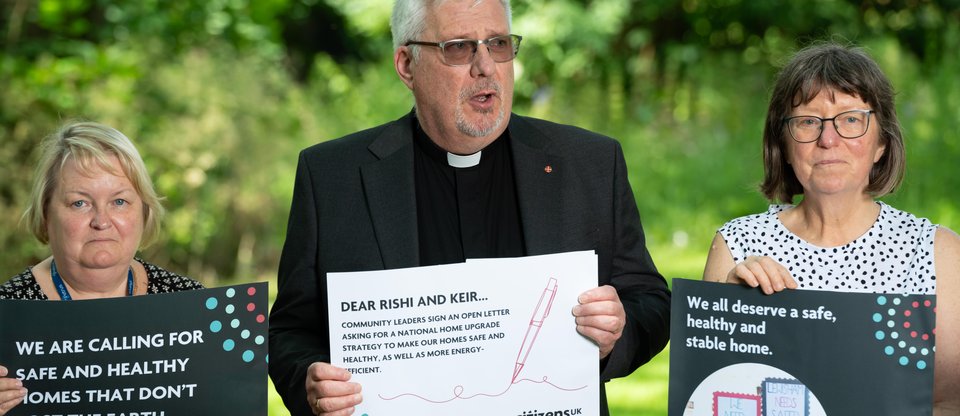 Three community leaders hold signs asking for safer homes. Rev Ian Rutherford remembers those who lost their lives to unfit homes.