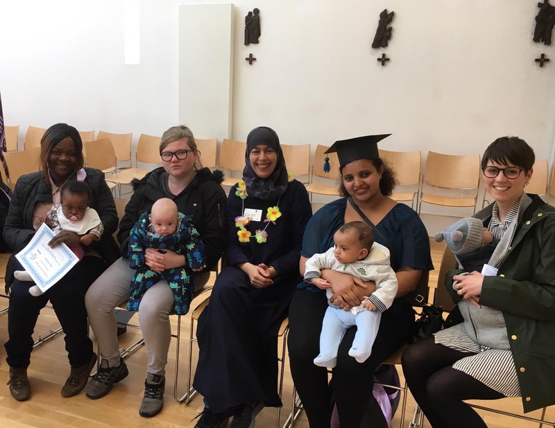 A group of parents and their babies are smiling at a Parent University session.