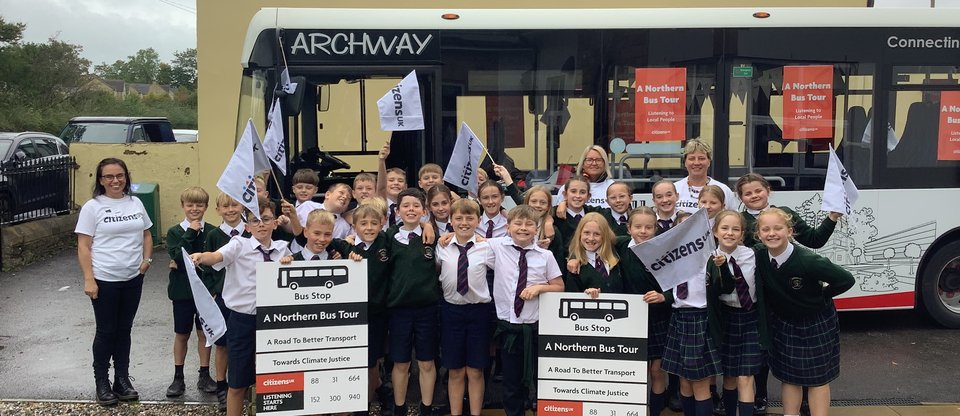 A group of school children stand in front of a bus.