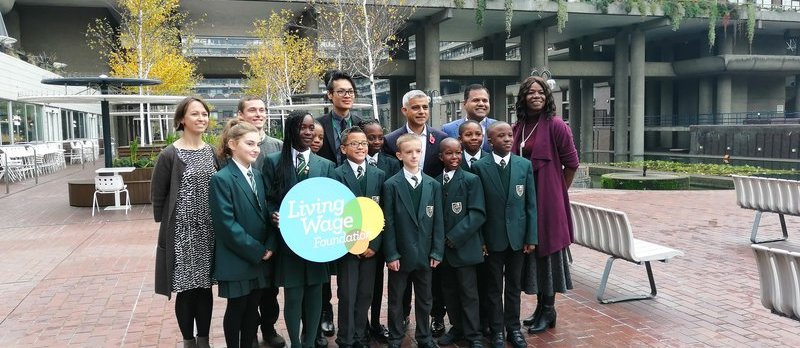 Primary school children pose with Mayor of London Sadiq Khan, holding a Living Wage Foundation sign.