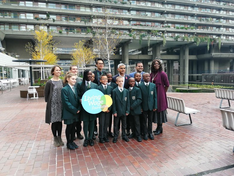 Primary school children pose with Mayor of London Sadiq Khan, holding a Living Wage Foundation sign.
