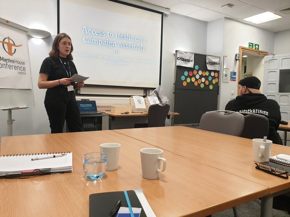 A campaigner speaks in a meeting room about their campaign for inclusive healthcare for trans and non binary people.