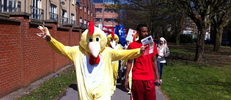 Man dressed in chicken costume, followed by supporters walking down the street, Citizens Cymru Wales action for Halal Nandos