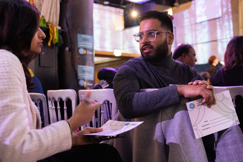 Two people are deep in conversation, both holding a pledge card